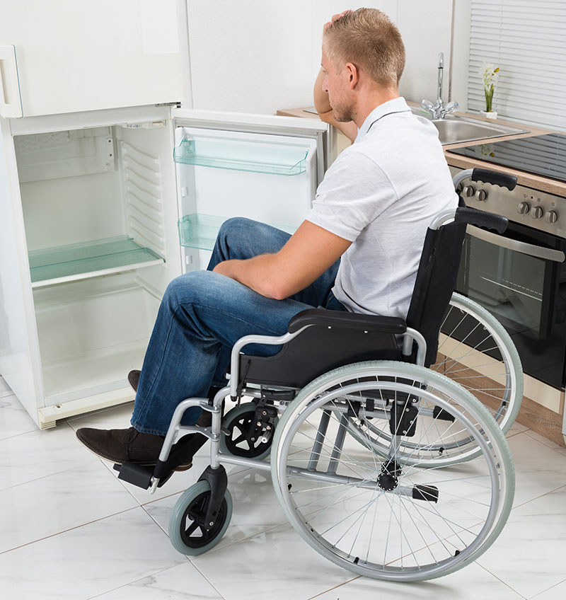 Young man in wheelchair looking at bare refrigerator.