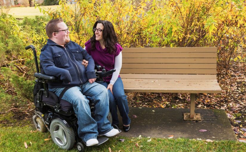 female case manager sitting next to young man in power chair on a bench